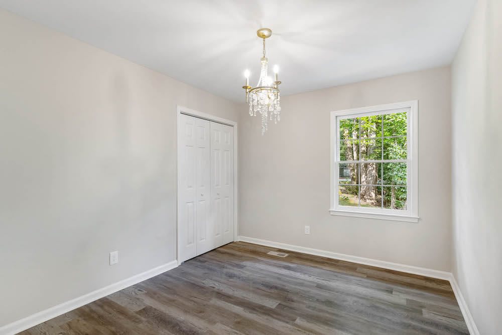 A bright, empty room with wooden floors and a chandelier.