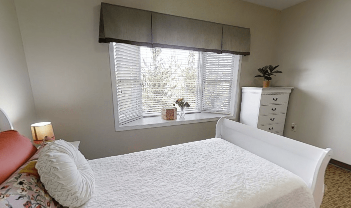 A bright bedroom with white bedding and a large window.