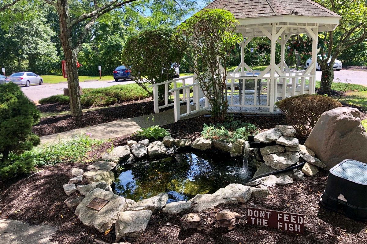 A serene garden scene featuring a pond surrounded by rocks, a wooden gazebo, and a small bridge.