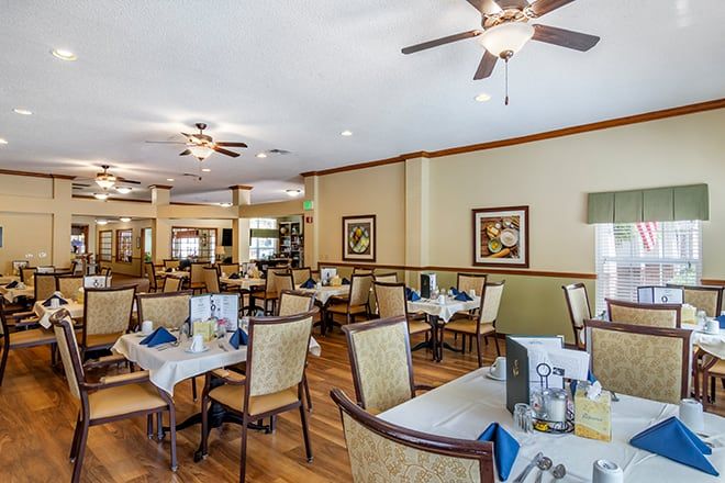 A spacious dining area in a restaurant featuring neatly arranged tables and chairs, warm lighting, and ceiling fans.