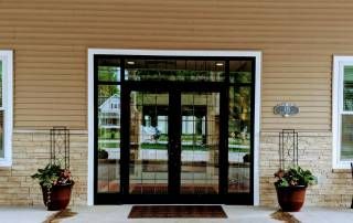 A building entrance with a glass door, flanked by potted plants.