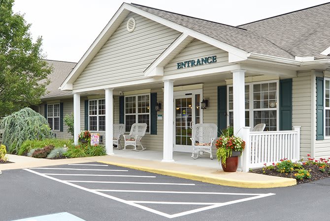 The entrance of a single-story building with a porch and parking area.