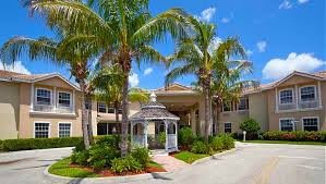 A sunny day view of a building entrance surrounded by palm trees and a small gazebo.