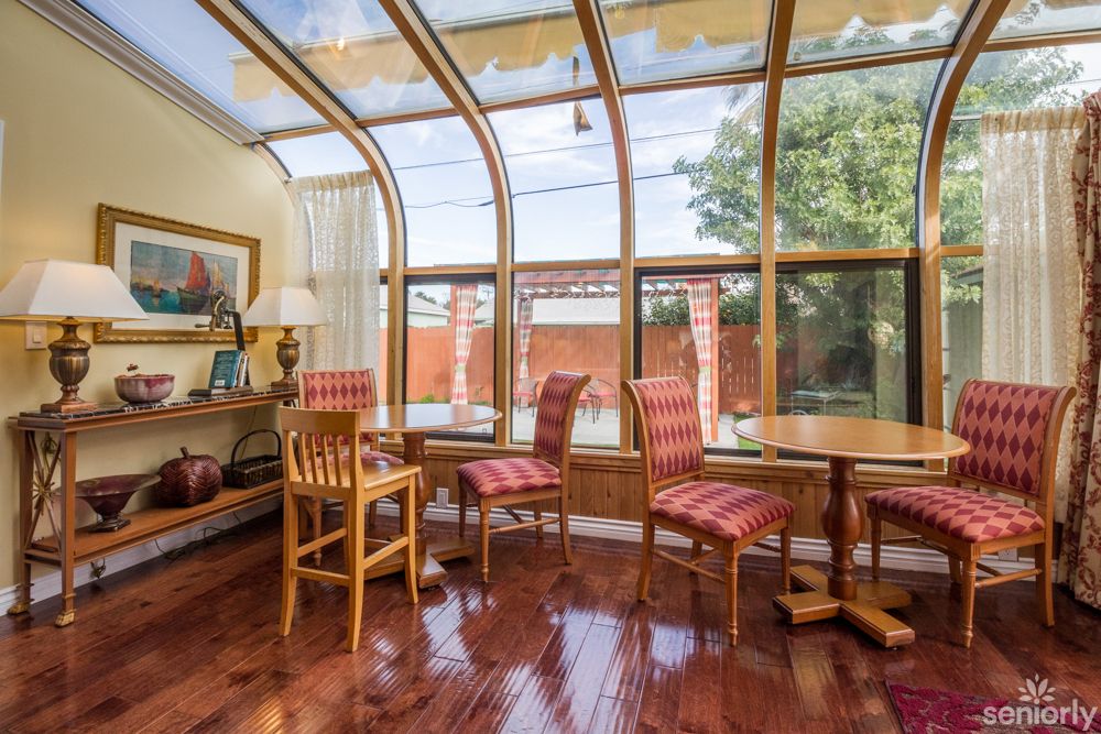 A cozy sunroom with a glass ceiling, featuring wooden floors and comfortable dining chairs.