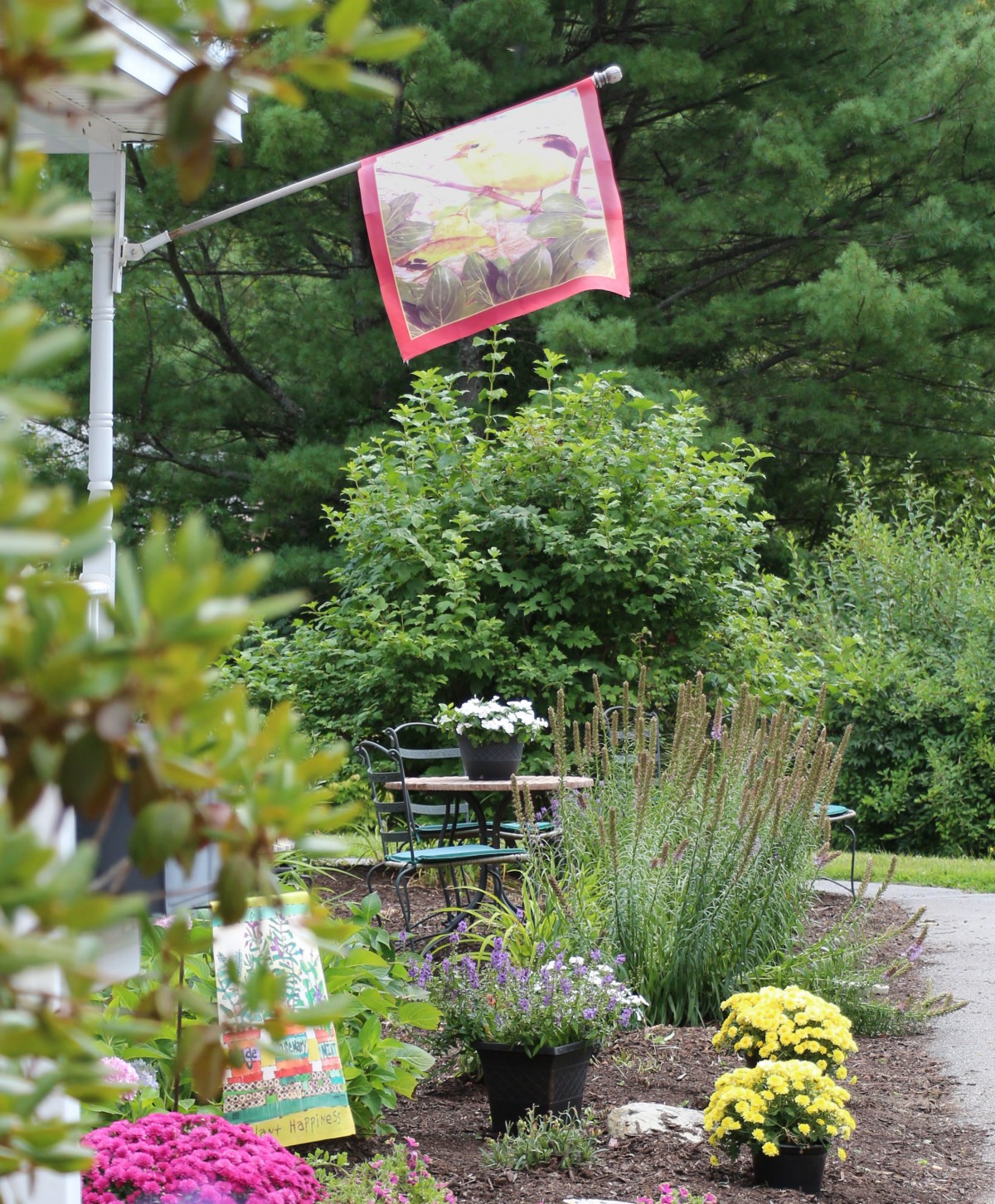 A colorful garden scene with a decorative flag, lush plants, and outdoor seating.