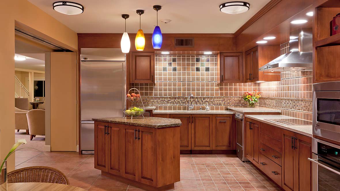 A modern kitchen featuring wood cabinets, an island, and colorful pendant lighting.