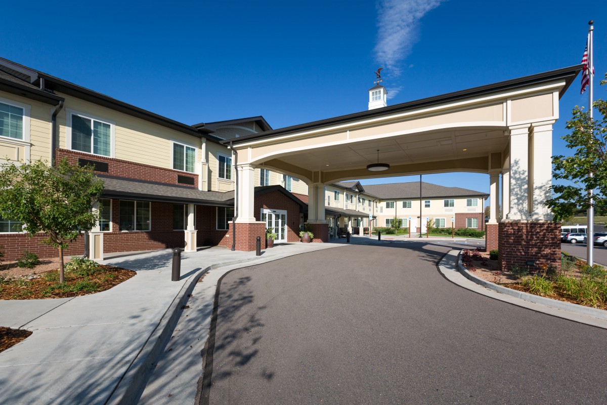 The image shows the entrance and driveway of a modern building on a clear day.