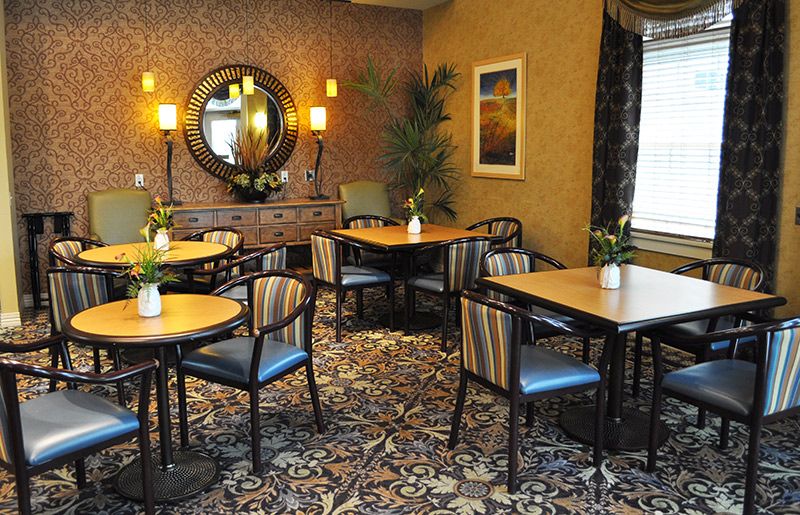 A cozy dining area with elegantly arranged tables and chairs, featuring a decorative mirror and green plants for ambiance.