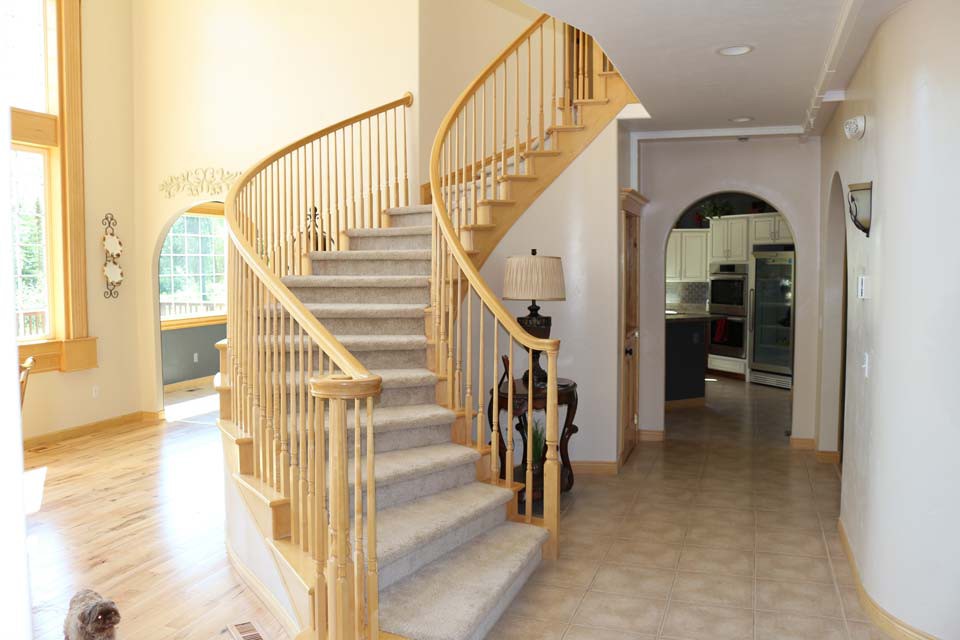 A bright, spacious home interior featuring a curved wooden staircase with carpeted steps.