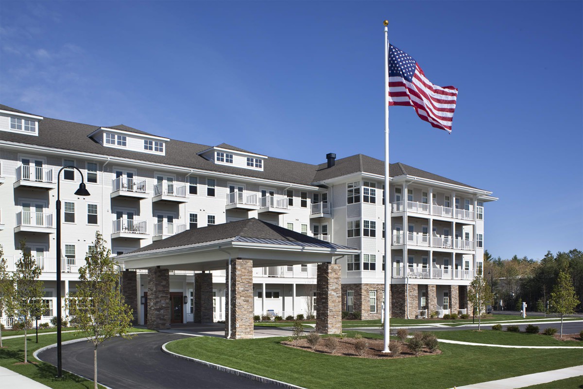 A four-story residential building with a covered entrance and a large American flag in front.