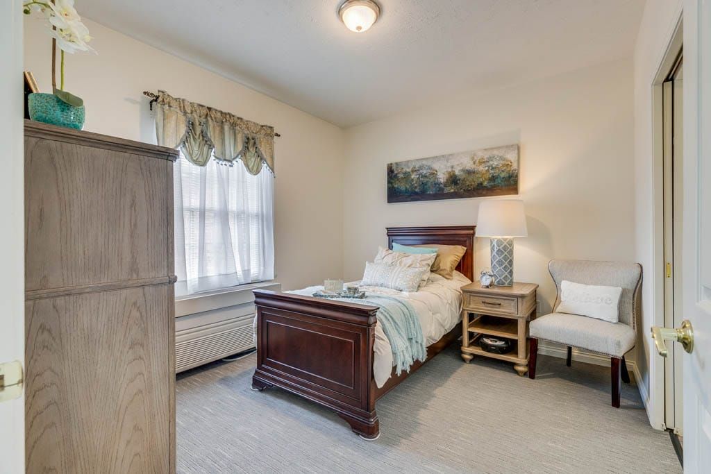 A cozy bedroom featuring a single bed, nightstand with a lamp, and a window adorned with curtains.