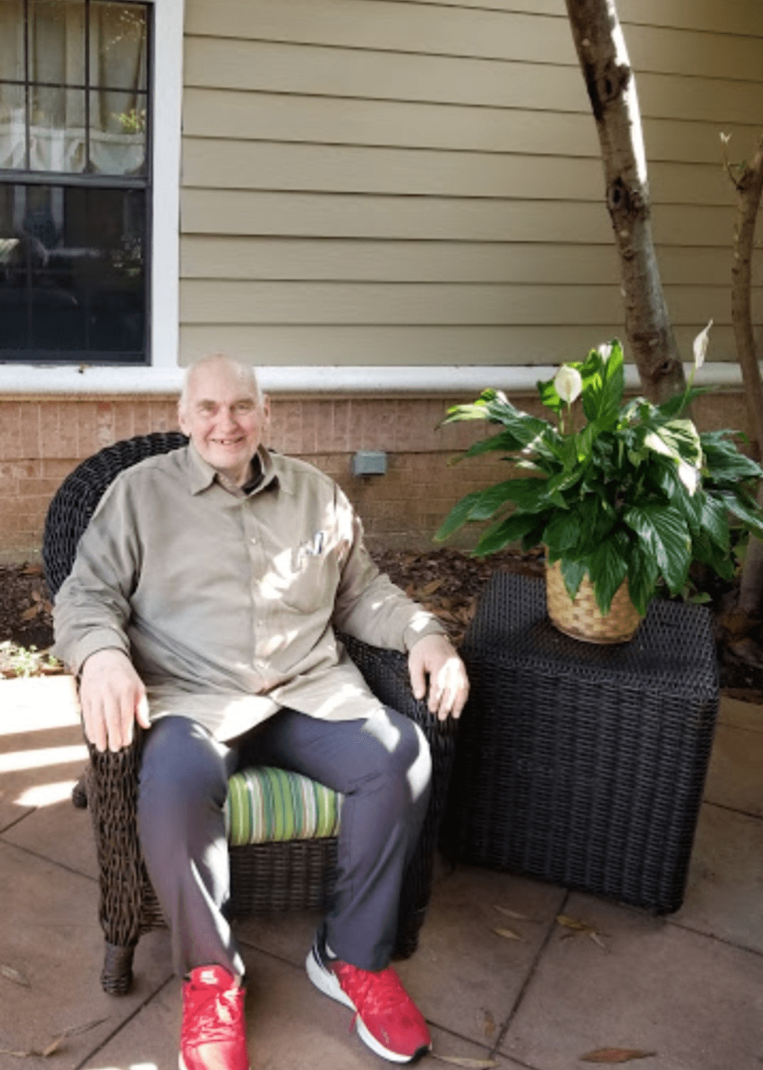 A man seated outdoors on a patio next to a potted plant.