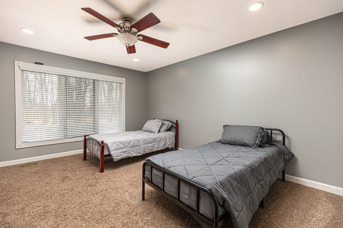 A modern bedroom with two twin beds featuring gray bedding, a ceiling fan, and gray walls.
