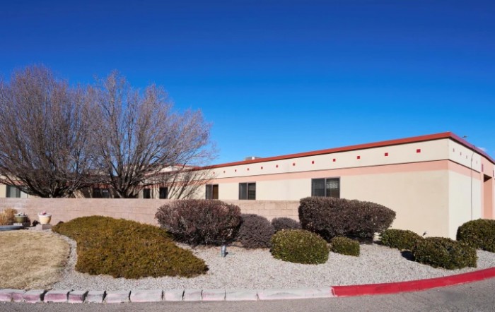 A single-story building surrounded by desert shrubbery under a clear blue sky.