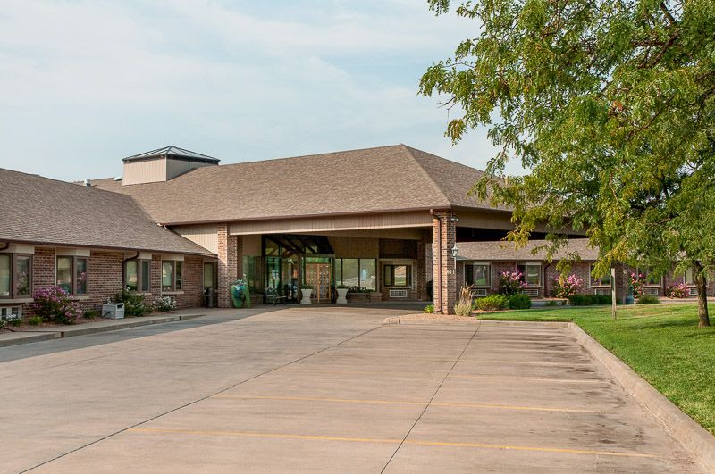 A view of a building entrance with a spacious driveway and surrounding greenery.