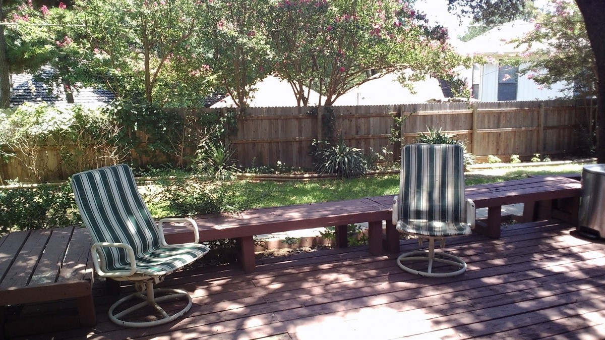 A sunny backyard patio with striped chairs and lush greenery.
