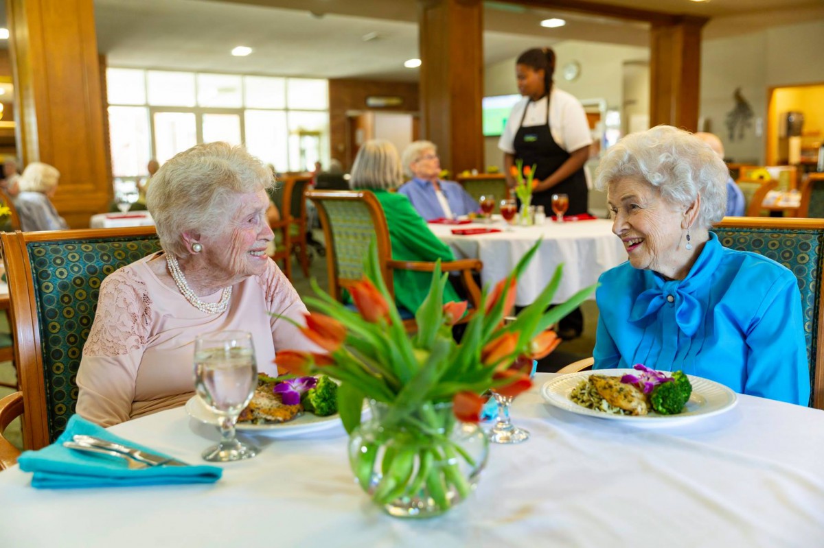 Two elderly women enjoying a meal and conversation in a dining area.