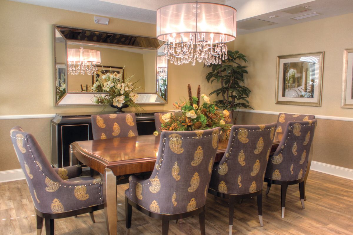 A stylish dining room featuring a wooden table surrounded by patterned chairs, adorned with an elegant chandelier and decorative elements.
