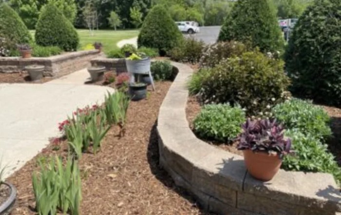 A beautifully landscaped garden with a stone walkway, potted plants, and outdoor seating on a sunny day.