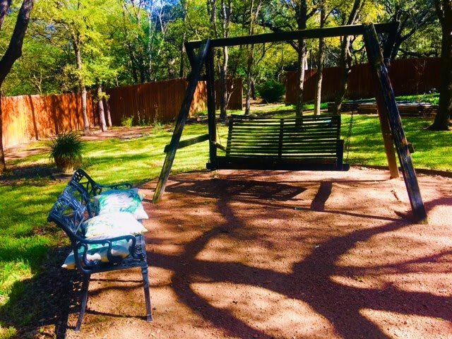 A peaceful park scene featuring a swing set and a bench under the shade of tall trees.