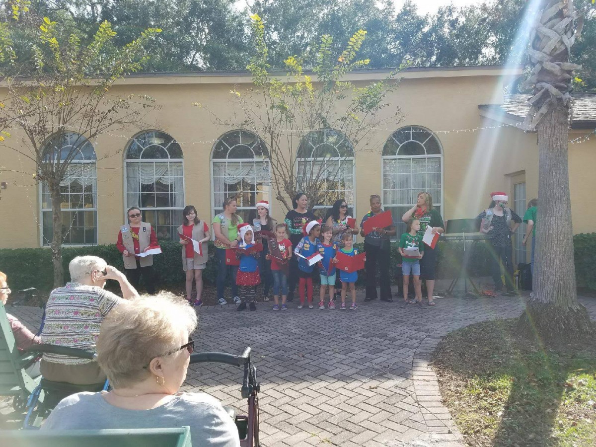 A group of people gathered outside in front of a building with arched windows on a sunny day.