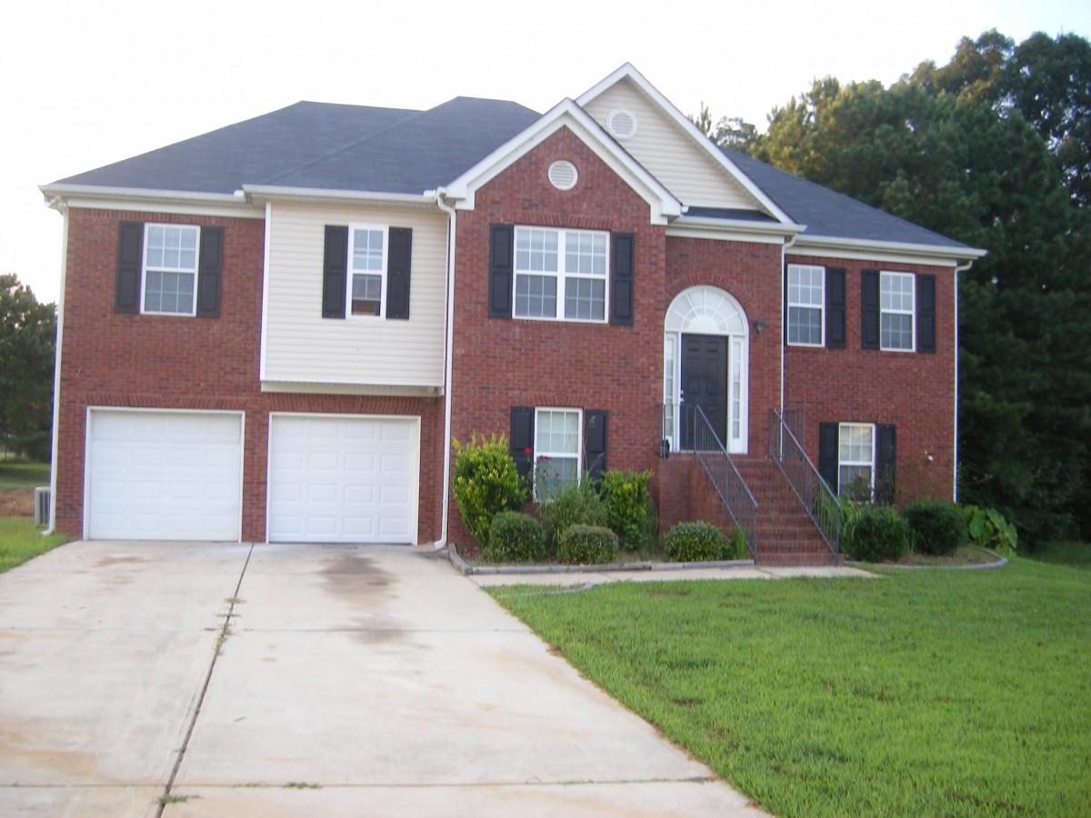A two-story suburban house with a brick exterior, driveway, and a green lawn.