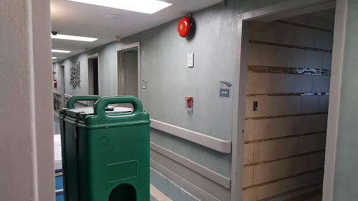 A view of a hospital corridor featuring an emergency alarm and a green trash can.