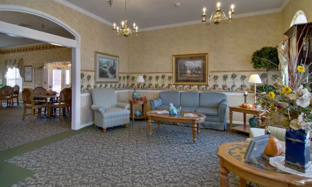 A traditionally decorated living room with sofas, armchairs, and a coffee table, featuring artwork and chandeliers.