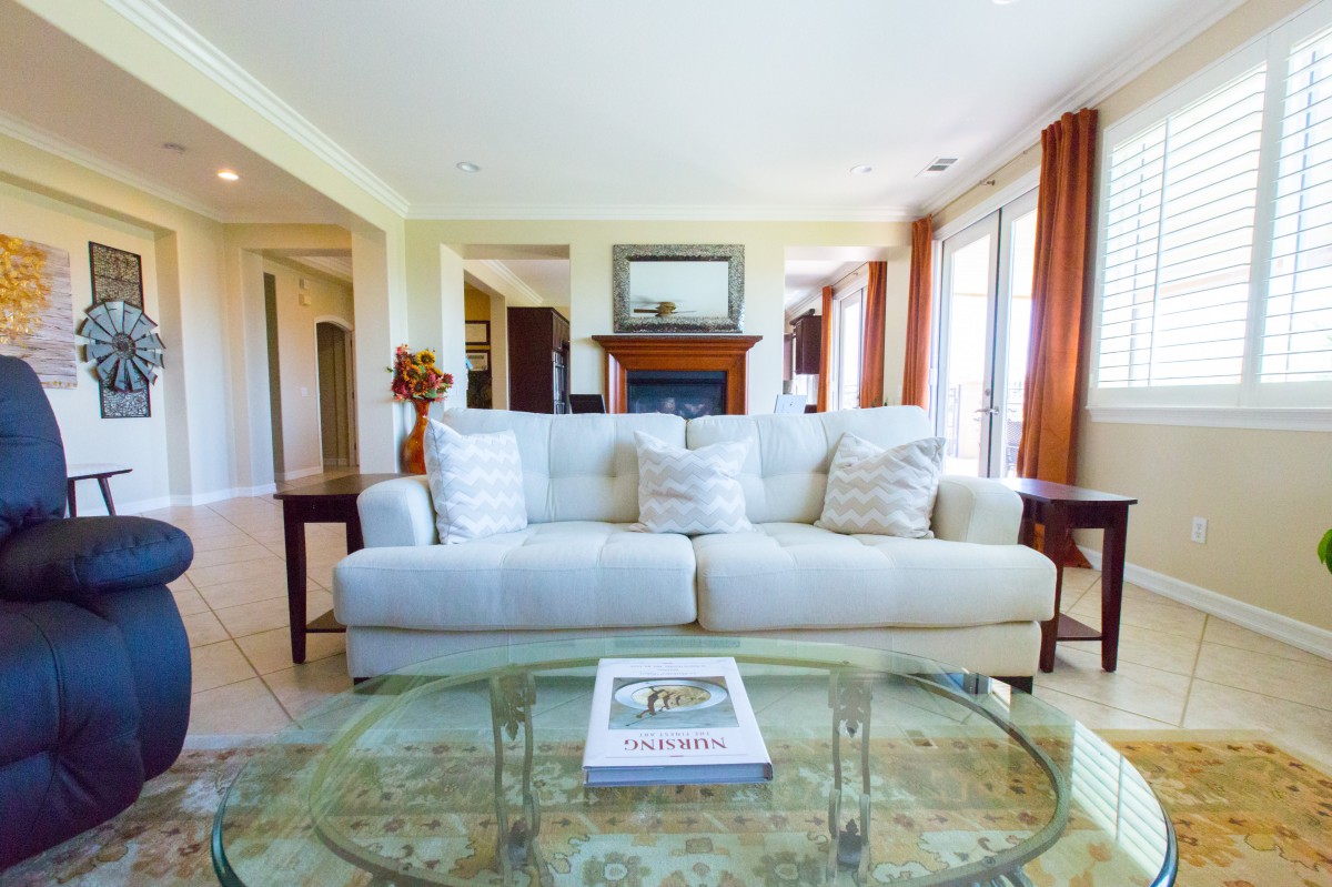 A cozy living room with a white sofa, glass coffee table, and large windows letting in natural light.