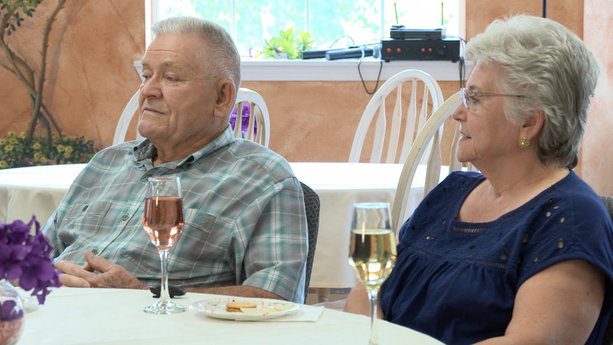 An elderly couple sitting at a table indoors, with wine glasses in front of them.