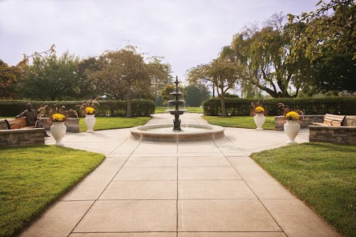 A serene garden pathway featuring a central fountain surrounded by lush greenery and decorative planters.