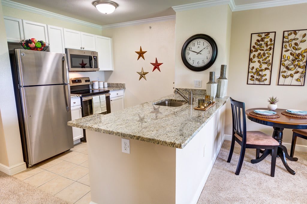 A modern kitchen with granite countertops and stainless steel appliances, featuring a wall clock and decorative stars.