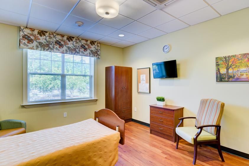 A cozy and well-lit bedroom with a bed, chair, wardrobe, and wall-mounted TV.