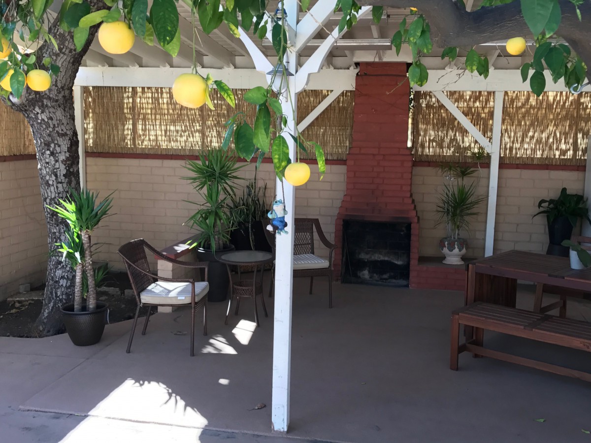 A cozy patio with outdoor seating, a fireplace, and lemon decorations under a shaded area.