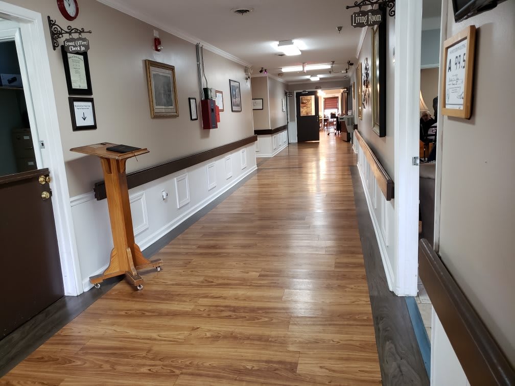 A long hallway with wooden floors in a healthcare facility, adorned with paintings on the walls.