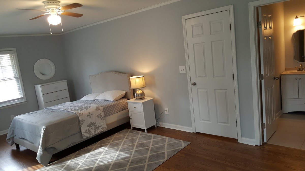 A minimalist bedroom with a bed, nightstand, and lamp next to a closed door.