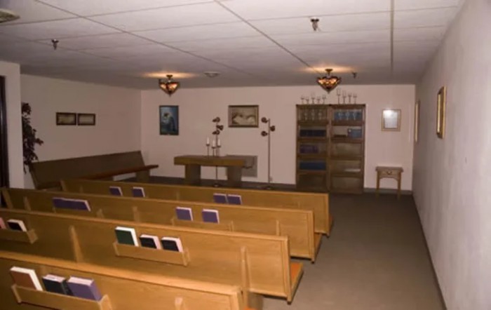 An indoor chapel with wooden benches and an altar, featuring religious decor and books.