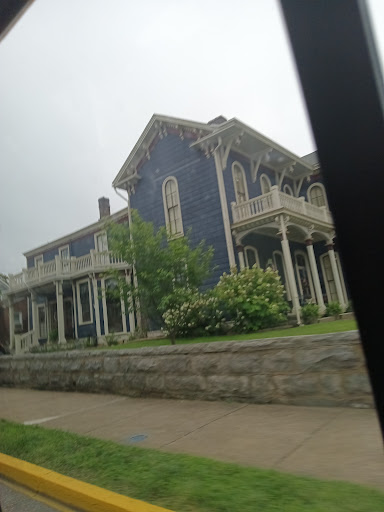 A beautifully crafted historic house with blue walls and elegant porch detailing, surrounded by lush greenery.