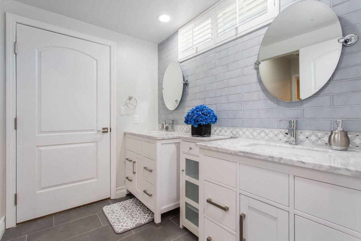 A modern bathroom featuring a double vanity with circular mirrors, decorated with a vase of blue flowers.