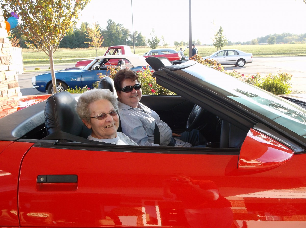 Two people sitting in a red convertible car enjoying a sunny day.