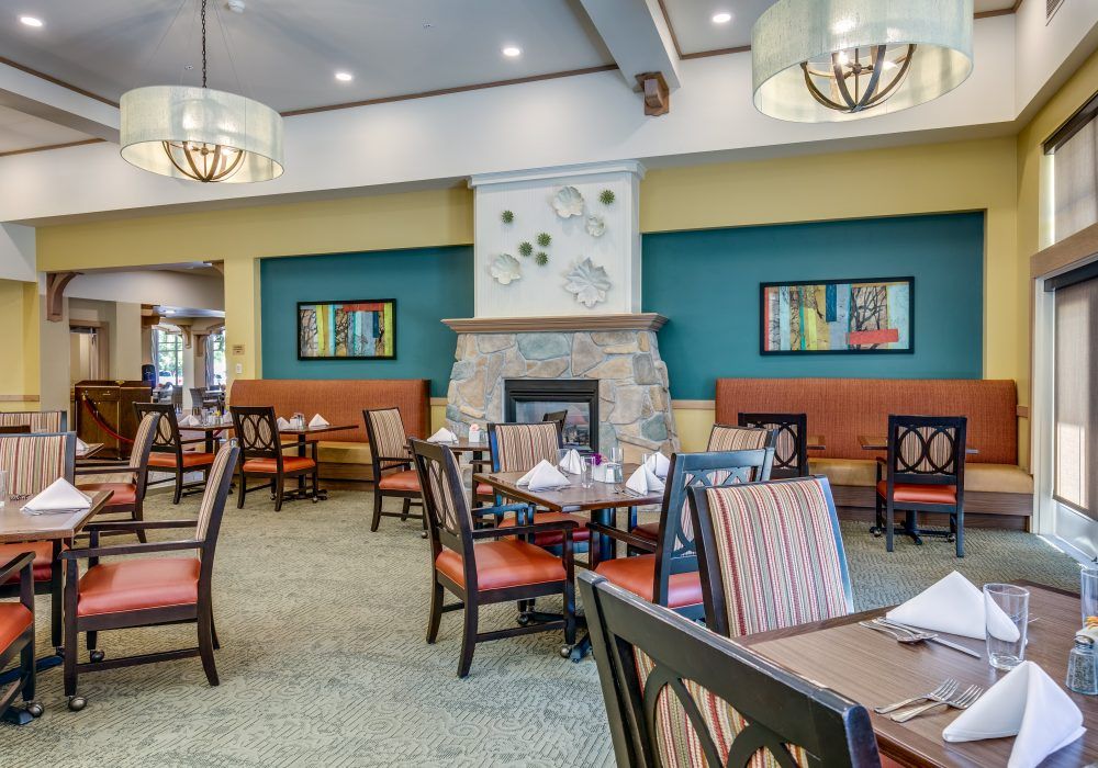 A cozy restaurant dining room with elegant interiors, featuring tables and chairs arranged around a central fireplace and colorful artwork on the walls.