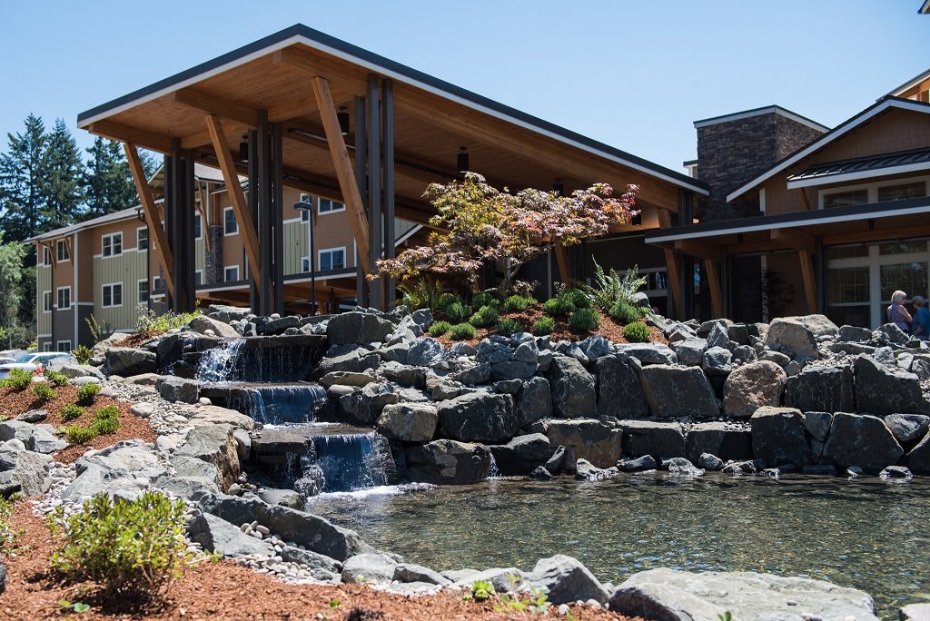 A modern building with a sloped roof is surrounded by a landscaped garden featuring a waterfall and pond.