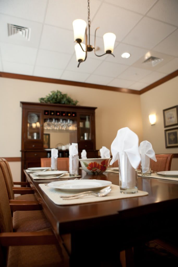 An elegantly set dining room table with neatly folded napkins and a wooden cabinet in the background.