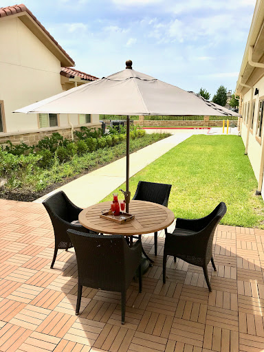 A cozy outdoor seating area featuring a round table with chairs under a white umbrella, surrounded by a lush green garden.
