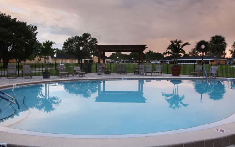 A serene outdoor swimming pool with surrounding patio furniture and a cloudy evening sky.