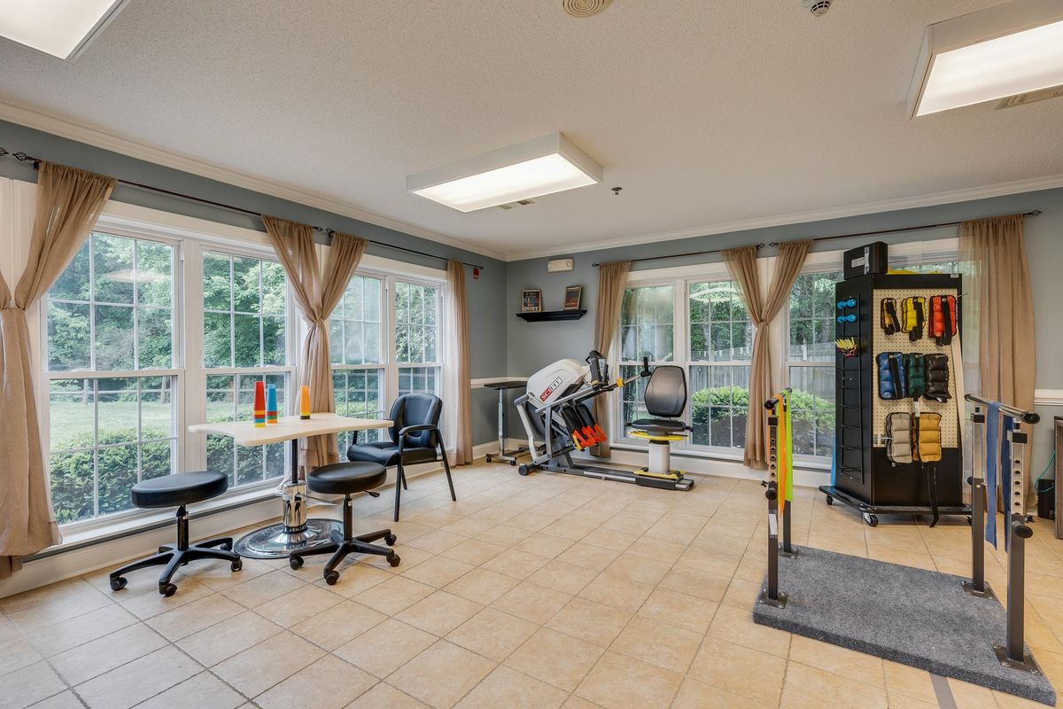A bright exercise room with various fitness equipment and large windows.