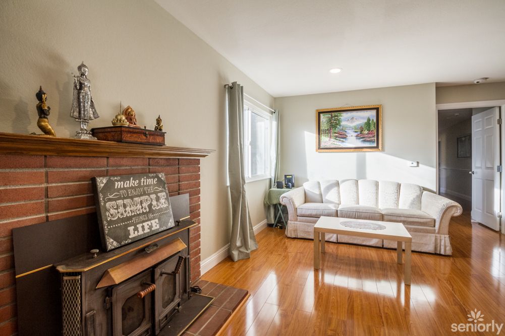 A cozy living room with a fireplace, sofa, and wooden flooring, featuring elegant decor and natural lighting.