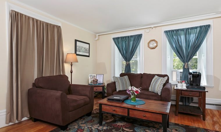 A cozy living room with a brown sofa and armchair, complemented by blue curtains and a wooden coffee table.