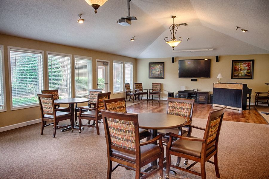 A spacious room with multiple tables and chairs, featuring a television and large windows.