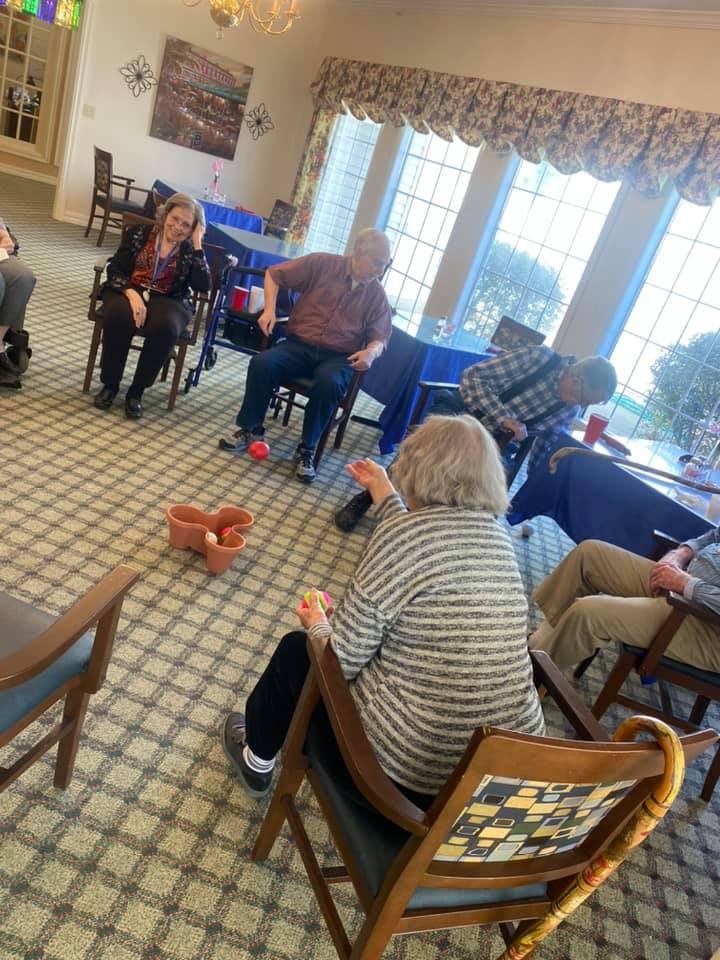 A group of seniors engaging in an indoor activity, seated in a circle.